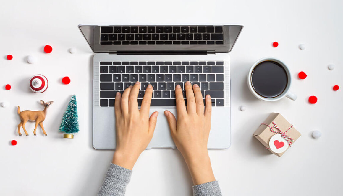 Top view of persons hands on laptop with white desk and Christmas decorations on each side.