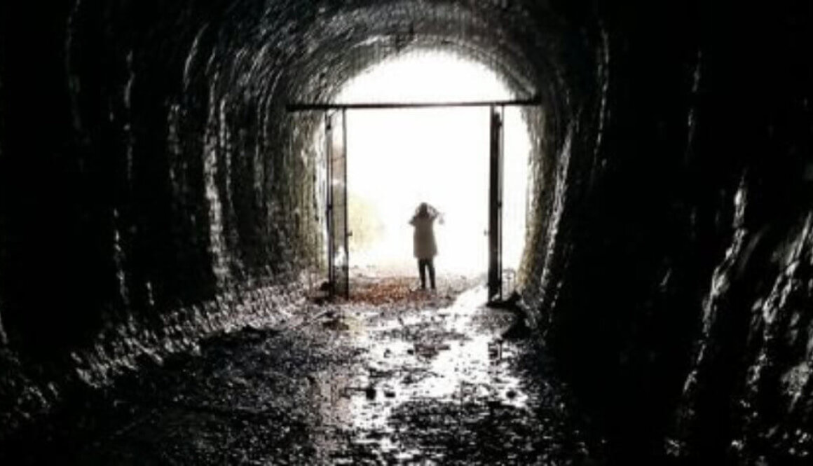 A person's silhouette against bright lights at the end of a dark tunnel.