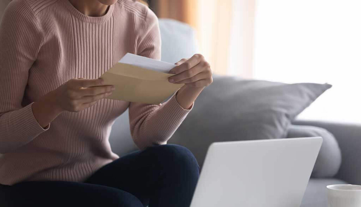 Woman sitting on couch with laptop on coffee table while holding a paper.