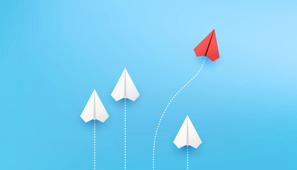 Paper airplane image of four airplanes fling upwards with white dotted lines behind them while one red airplane goes on a curved path.