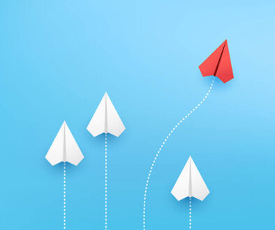 Paper airplane image of four airplanes fling upwards with white dotted lines behind them while one red airplane goes on a curved path.