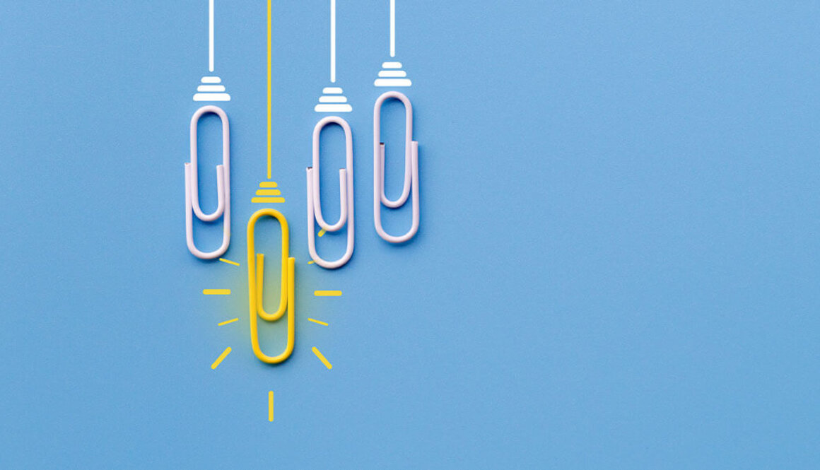 Four paperclips laying on blue background while one bright yellow paperclip hangs lower.