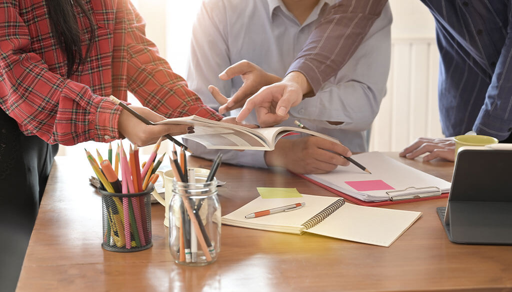 print-marketing-design Work team looking and pointing to an open book.